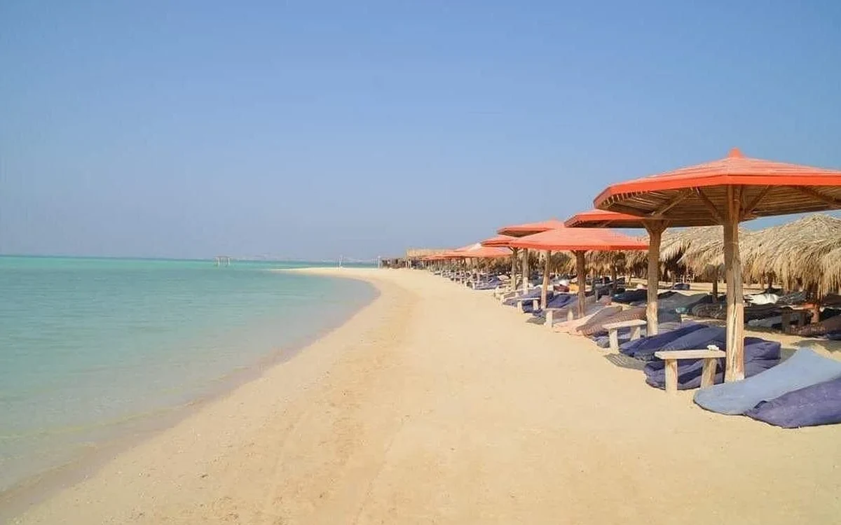 Sandy beach with shaded sun loungers beside calm water