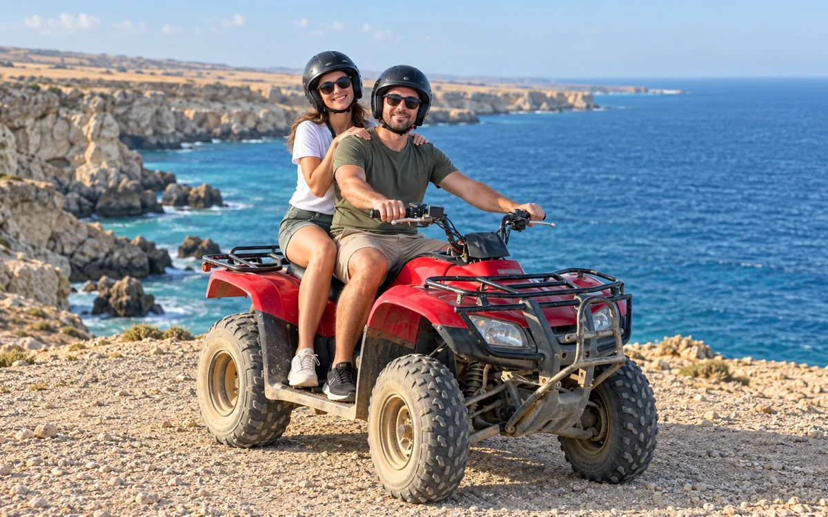 Zwei Erwachsene mit Helmen auf einem roten Quad an felsigen Küstenklippen
