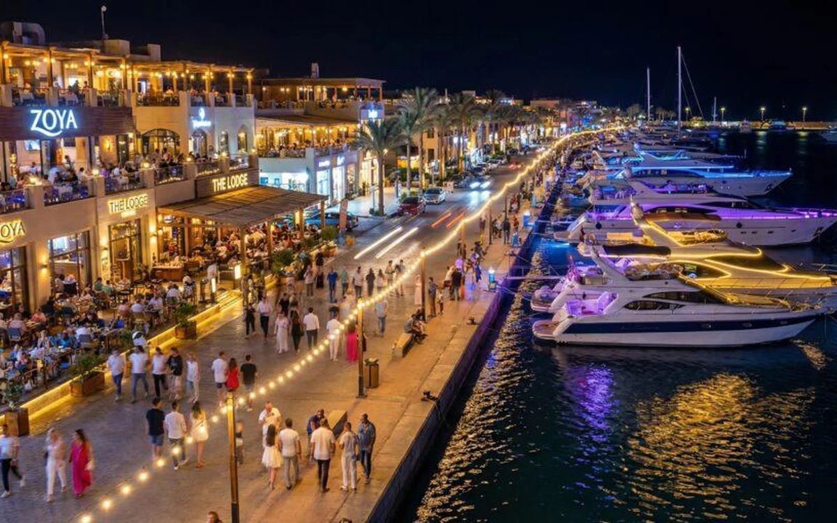 قوارب راسية بجانب ممشى مضاء بالكامل على الواجهة البحرية ليلًا