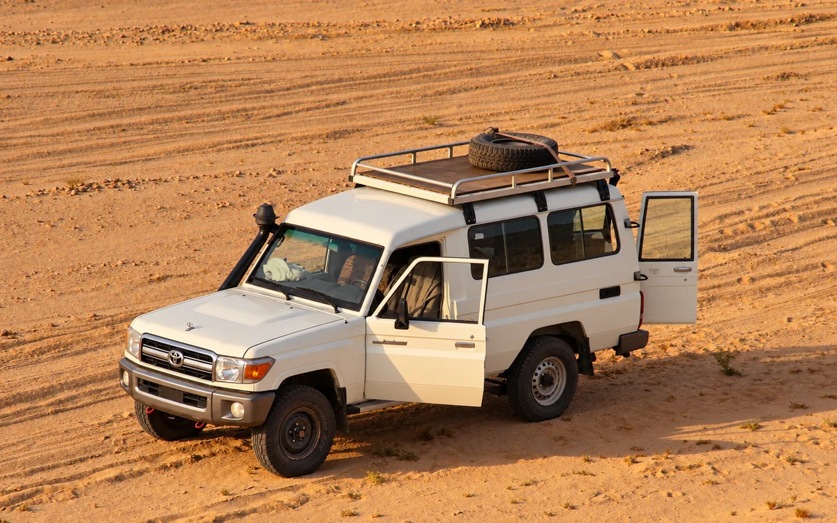 White off-road jeep with a roof rack parked on the desert sand near Hurghada in late-afternoon light